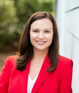 Woman smiling in a red blazer outside.